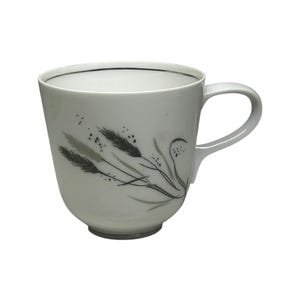 May include: White ceramic mug with a curved handle. The mug features a black and gray wheat stalk design on the side and a thin black line around the rim. The mug is suitable for hot or cold beverages.