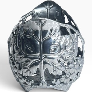 May include: A polished silver-toned metal basket featuring an intricate openwork design of grape leaves and clusters of grapes. The structure is formed by interconnected vine-like branches that create a rounded, bowl-shaped container with a sturdy base.