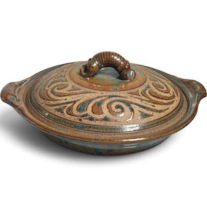 May include: A round, glazed ceramic casserole dish with a matching lid. The piece features a mottled brown and blue finish with embossed, swirling patterns across the lid and a curved, textured handle centered on top.