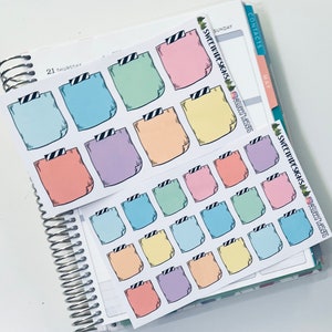 May include: A sheet of colorful planner stickers with a folded paper design. The stickers are in various pastel colors, including pink, blue, green, yellow, and purple. Each sticker has a black and white striped design at the top.