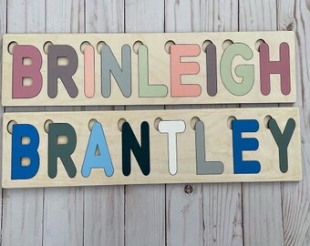May include: Two wooden puzzle pieces with the names Brinleigh and Brantley spelled out in colorful letters. The letters are painted in various shades of blue, green, pink, and gray.