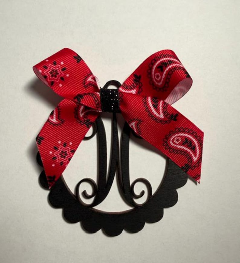 Pu&ograve; includere: Un monogramma nero con un fiocco rosso paisley. Il monogramma ha la forma della lettera "M" ed &egrave; circondato da un bordo smerlato. Il fiocco &egrave; realizzato in nastro rosso con un motivo paisley bianco.