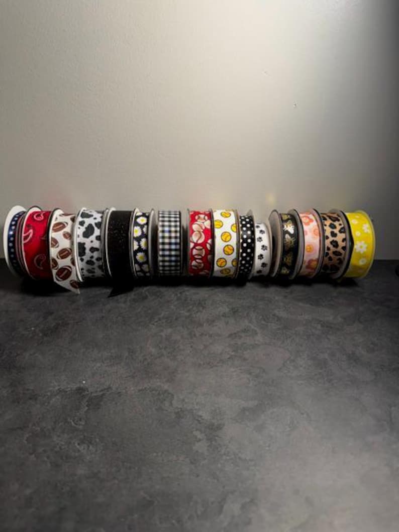 Pu&ograve; includere: Una collezione di rocchetti di nastro decorativo con vari motivi, tra cui paisley, chicchi di caff&egrave;, stampa mucca, margherite, quadretti vichy, palline da baseball e impronte di zampe. I nastri sono in vari colori, come rosso, nero, bianco e giallo.