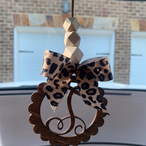 Pu&ograve; includere: Un ciondolo per auto in legno con bordo smerlato, con un fiocco con stampa leopardata e un'iniziale in legno. Il ciondolo &egrave; sospeso da perline di legno e uno spago, progettato per essere appeso allo specchietto retrovisore di un'auto.