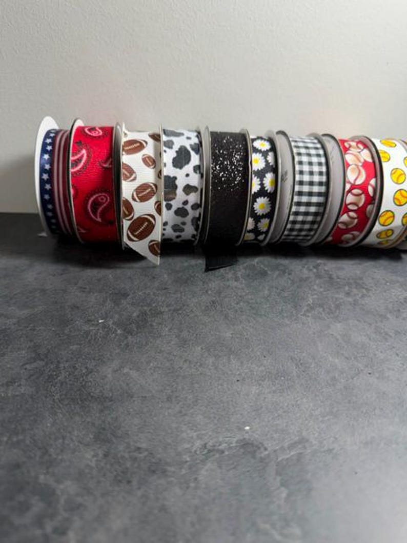 Pu&ograve; includere: Una collezione di rocchetti di nastro decorativo con vari motivi. I disegni includono stelle, paisley, palloni da football, stampa mucca, glitter, margherite, quadretti, palline da baseball e da tennis. I nastri sono su rocchetti bianchi.