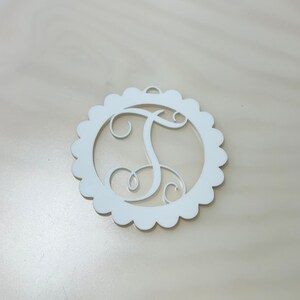 Pu&ograve; includere: Monogramma in legno bianco con la lettera "T" all'interno di un cerchio smerlato. La lettera corsiva ha un piccolo anello per appendere. Design semplice ed elegante, adatto a varie decorazioni.