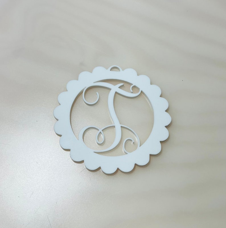 Pu&ograve; includere: Monogramma in legno bianco con la lettera "T" all'interno di un cerchio smerlato. La lettera corsiva ha un piccolo anello per appendere. Design semplice ed elegante, adatto a varie decorazioni.