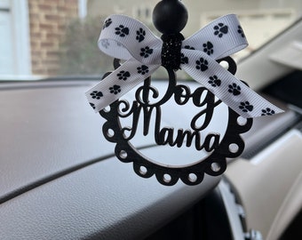 Può includere: Ciondolo per auto nero e bianco con un nastro con impronte di zampa e le parole "Dog Mama" in un carattere decorativo.
