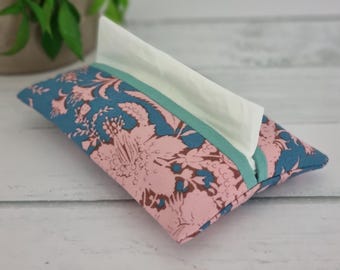 May include: A fabric tissue holder with a teal and pink floral pattern. White tissues are visible at the top. The holder has a teal ribbon trim. The floral design is a repeating pattern.