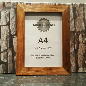 Peut inclure: Cadre photo en bois A4 fabriqu&eacute; &agrave; partir de bois de r&eacute;cup&eacute;ration. Le cadre est de couleur marron chaud et pr&eacute;sente le texte "MADE by RUSTY" et "A4 21 X 29,7 cm". Le cadre est fait &agrave; la main.