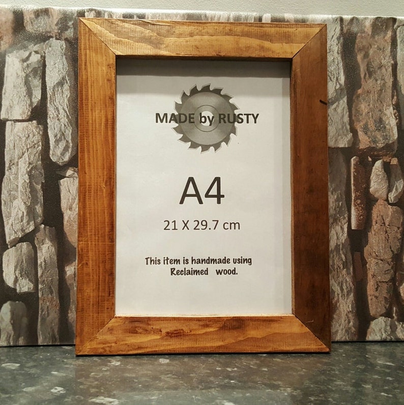 Peut inclure: Cadre photo en bois A4 fabriqu&eacute; &agrave; partir de bois de r&eacute;cup&eacute;ration. Le cadre est de couleur marron chaud et pr&eacute;sente le texte "MADE by RUSTY" et "A4 21 X 29,7 cm". Le cadre est fait &agrave; la main.