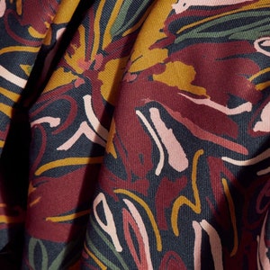 May include: Close-up of a fabric with a colourful abstract pattern. The fabric is a dark red colour with yellow, pink, and green accents. The pattern is made up of swirls and lines.