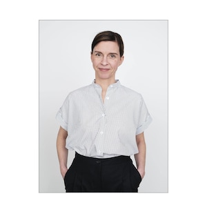 May include: A woman wearing a white and black striped button-down shirt with a mandarin collar and black pants.