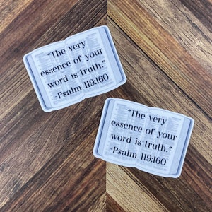 Op de afbeelding: Twee witte stickers met een bijbelvers erop gedrukt. Het vers is "De essentie van uw woord is waarheid." -Psalm 119:160.