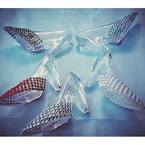 May include: Five clear glass high-heeled shoes with rhinestones. The shoes have different colored rhinestones, including red, white, and silver.