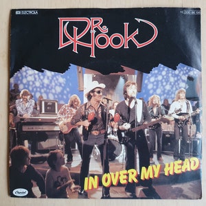 May include: A vintage vinyl record cover featuring a band called "Dr. Hook" with the title "In Over My Head". The cover features a photo of the band performing on stage with a crowd of people in the background.