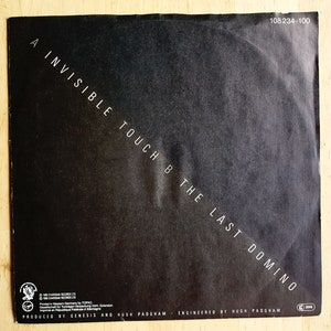 May include: Black and white record label with the text "A Invisible Touch B The Last Domino" and the text "Produced by Genesis and Hugh Padgham - Engineered by Hugh Padgham".