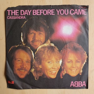 Peut inclure: Un single 45 tours vinyle d'ABBA, avec la chanson "The Day Before You Came" et le titre "Cassandra". La pochette du disque présente un gros plan des membres du groupe, sur un fond rose et blanc.