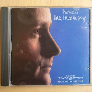 Może przedstawiać: Pudełko na płytę CD z niebieskim tłem i profilem twarzy mężczyzny. Widoczny jest tekst "Phil Collins" i "Hello, I Must Be Going!". Na pudełku znajduje się również tekst "I DON'T CARE ANYMORE" i "YOU CAN'T HURRY LOVE."