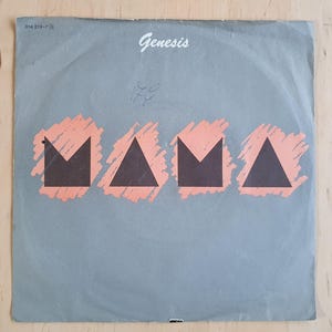 May include: A gray vinyl record with the word "Genesis" printed in white at the top and the word "MAMA" printed in black with a pink background. The record is a 7-inch single.