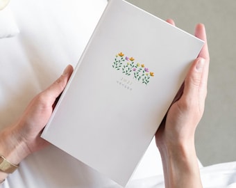 May include: A white planner with a minimalist floral illustration featuring small yellow, purple, and orange flowers with green stems. The cover displays the year 2027 printed in a small, simple font directly below the floral design.