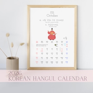 Peut inclure: Calendrier coréen Hangul 2026 encadré. La page d'octobre du calendrier est affichée, avec du texte et des illustrations coréennes. Le calendrier est dans un cadre en bois clair, avec une surface rose au premier plan.