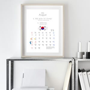 Könnte beinhalten: Ein gerahmter Wandkalender für August 2027 mit koreanischem Text, einer Grafik der südkoreanischen Flagge und einem Datumsraster. Das Design enthält kleine Illustrationen einer Sonne und einer Person sowie englischen und koreanischen Text.