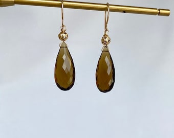 May include: A pair of gold earrings with teardrop-shaped brown gemstone drops and textured gold beads.