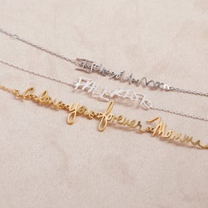 May include: Three delicate chain necklaces featuring cursive metal lettering. The top silver necklace reads I love you mom, the middle silver necklace reads FALL RISK, and the bottom gold necklace reads I love you forever Momma.