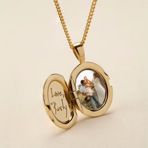 May include: A gold-toned oval locket pendant on a matching chain. The locket is open, revealing a photograph of two people embracing on the right side and the handwritten text "Love, Rusty" engraved on the left interior panel of the metal casing.