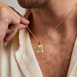 May include: A gold-toned rectangular pendant necklace featuring three horizontal chevron-shaped rows of small, vibrant green gemstones. The pendant hangs from a delicate gold-toned chain resting against the neck.
