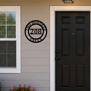 May include: A circular black metal address sign mounted on a wall, featuring the number 208 in the center with the text TWO HUNDRED arched above and GREEN arched below, all contained within a circular frame with horizontal bars.