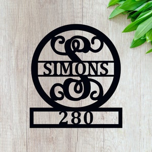 May include: Black metal house number sign with a circle featuring a stylized letter "S" and the name "SIMONS" across the center. The number "280" is displayed on a rectangular plate below the circle.