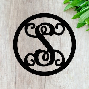 May include: Black metal monogram with a decorative letter S in a circle. The monogram is on a wood background.