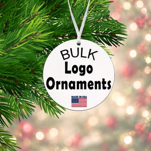 May include: A round white ornament hanging from a white ribbon. The ornament features the black text BULK Logo Ornaments and a small American flag icon with the text MADE IN USA printed in black below the flag.