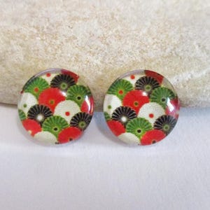 May include: A pair of round stud earrings with a colorful floral pattern. The earrings feature a design of red, green, black, and white fan-shaped elements. The earrings are set against a white background.