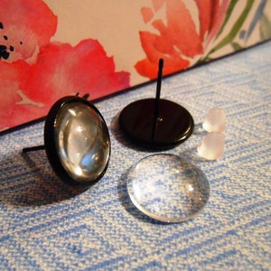 May include: A pair of black and clear glass earrings with a post and butterfly back. The earrings are on a blue and white patterned surface.