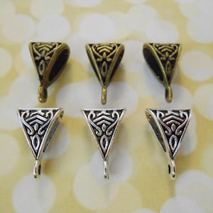May include: Six metal pendant bails in two styles. Three are bronze-toned, and three are silver-toned. Each bail is triangular with an ornate, openwork design and a small loop at the bottom for attaching a chain or cord.