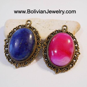 May include: Two oval-shaped pendants with ornate bronze frames. The left pendant features a blue lapis lazuli stone, while the right pendant features a pink and white agate stone.