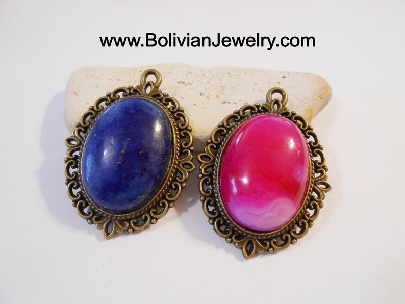 May include: Two oval-shaped pendants with ornate bronze frames. The left pendant features a blue lapis lazuli stone, while the right pendant features a pink and white agate stone.