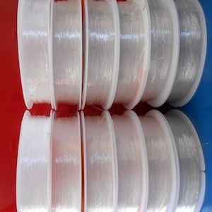 May include: Eight spools of clear elastic thread wound on white plastic spools. The spools are arranged in two rows of four, with the top row slightly offset from the bottom row.