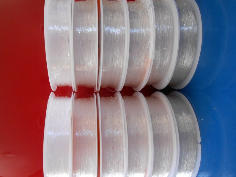 May include: Eight spools of clear elastic thread wound on white plastic spools. The spools are arranged in two rows of four, with the top row slightly offset from the bottom row.