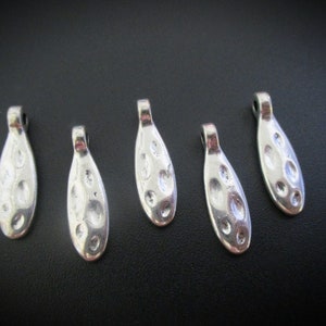 May include: Six silver-toned pendant charms with a textured, oval shape. Each charm has a loop at the top for attaching to a necklace or bracelet.