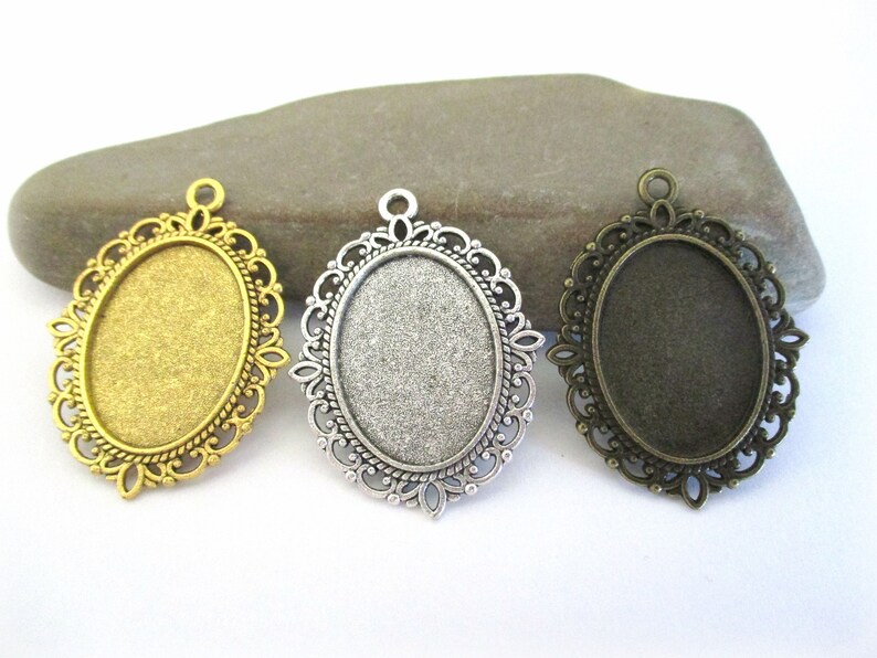 May include: Three oval-shaped metal pendant trays with ornate filigree designs. The trays are gold, silver, and bronze in colour.