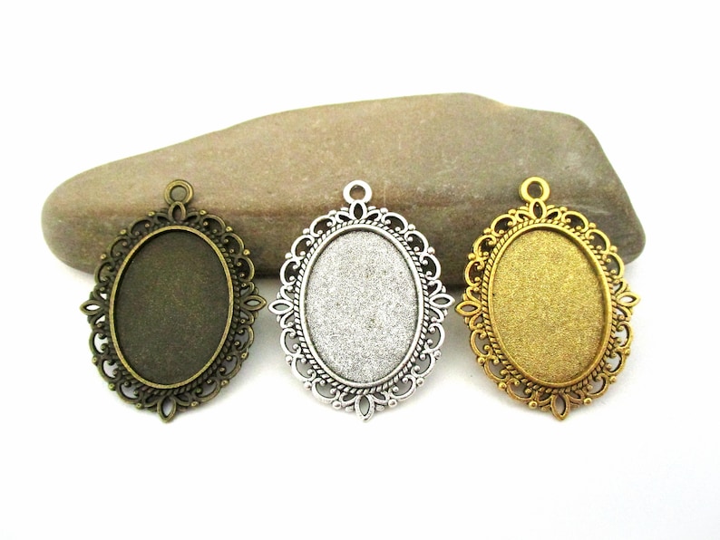 May include: Three oval-shaped pendant trays with ornate metal frames. The frames are in bronze, silver, and gold finishes.