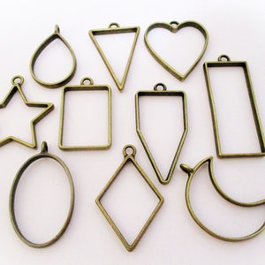May include: A set of ten different metal pendant frames in various shapes, including a star, heart, oval, teardrop, crescent moon, rectangle, triangle, diamond, and two different rectangular shapes. The frames are all made of a gold-toned metal.