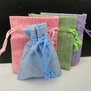 May include: Four small drawstring bags made of burlap fabric. The bags are in different colors: pink, light blue, green, and lavender. The bags are all tied with matching colored cords.