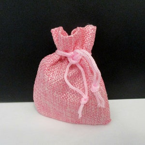 May include: A pink burlap drawstring bag with a pink ribbon closure.
