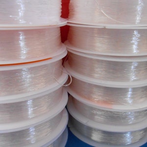 May include: Close-up of multiple spools of clear, translucent thread wound around white plastic bobbins. The spools are stacked on top of each other.