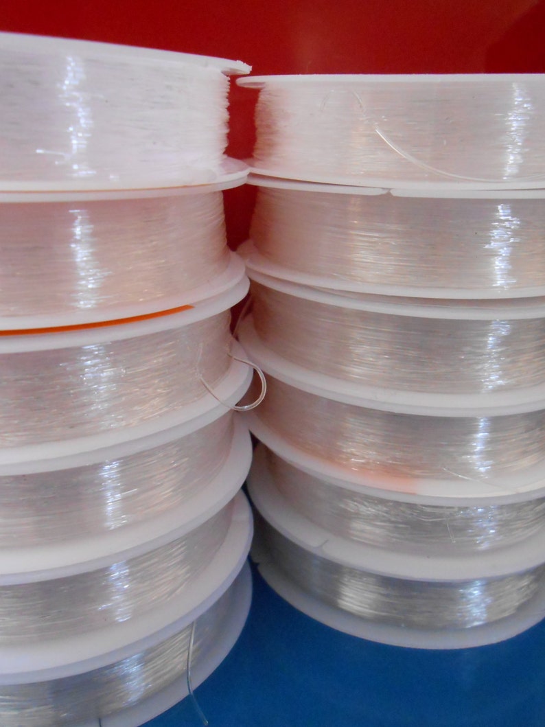 May include: Close-up of multiple spools of clear, translucent thread wound around white plastic bobbins. The spools are stacked on top of each other.
